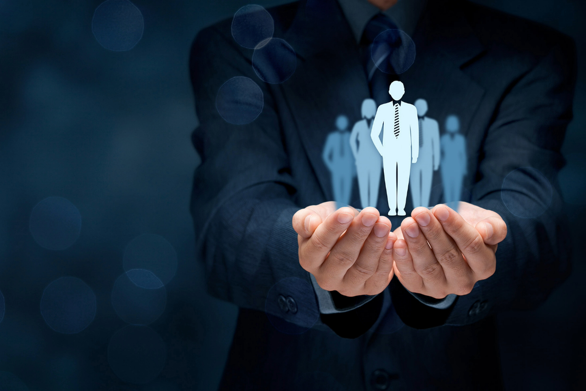 a business person in a navy suit holding imaginary blue figurines of business people in their hands on a blue background with blurry bubbles 