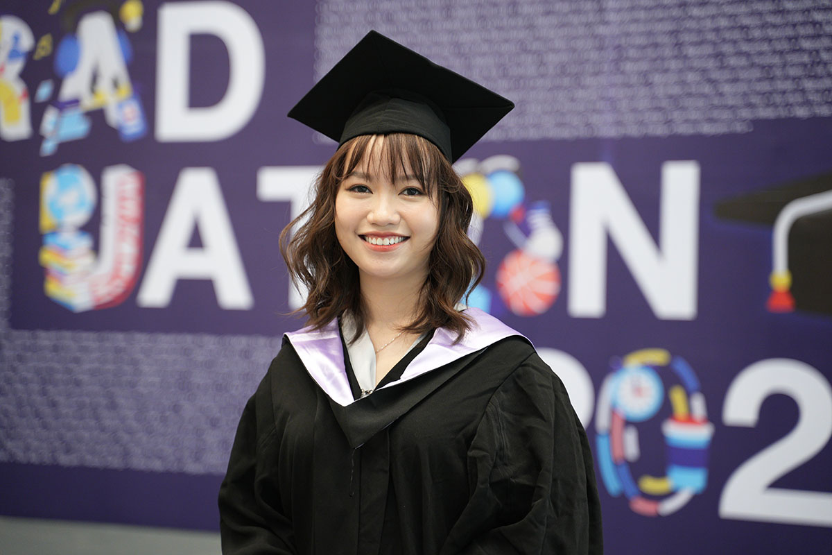 an Asian women wearing graduation robe smiling