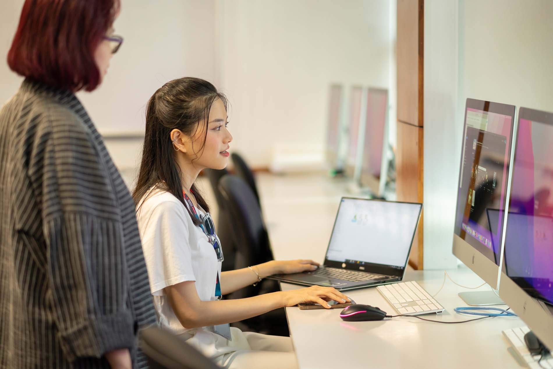 Female student using computer while other female student watching