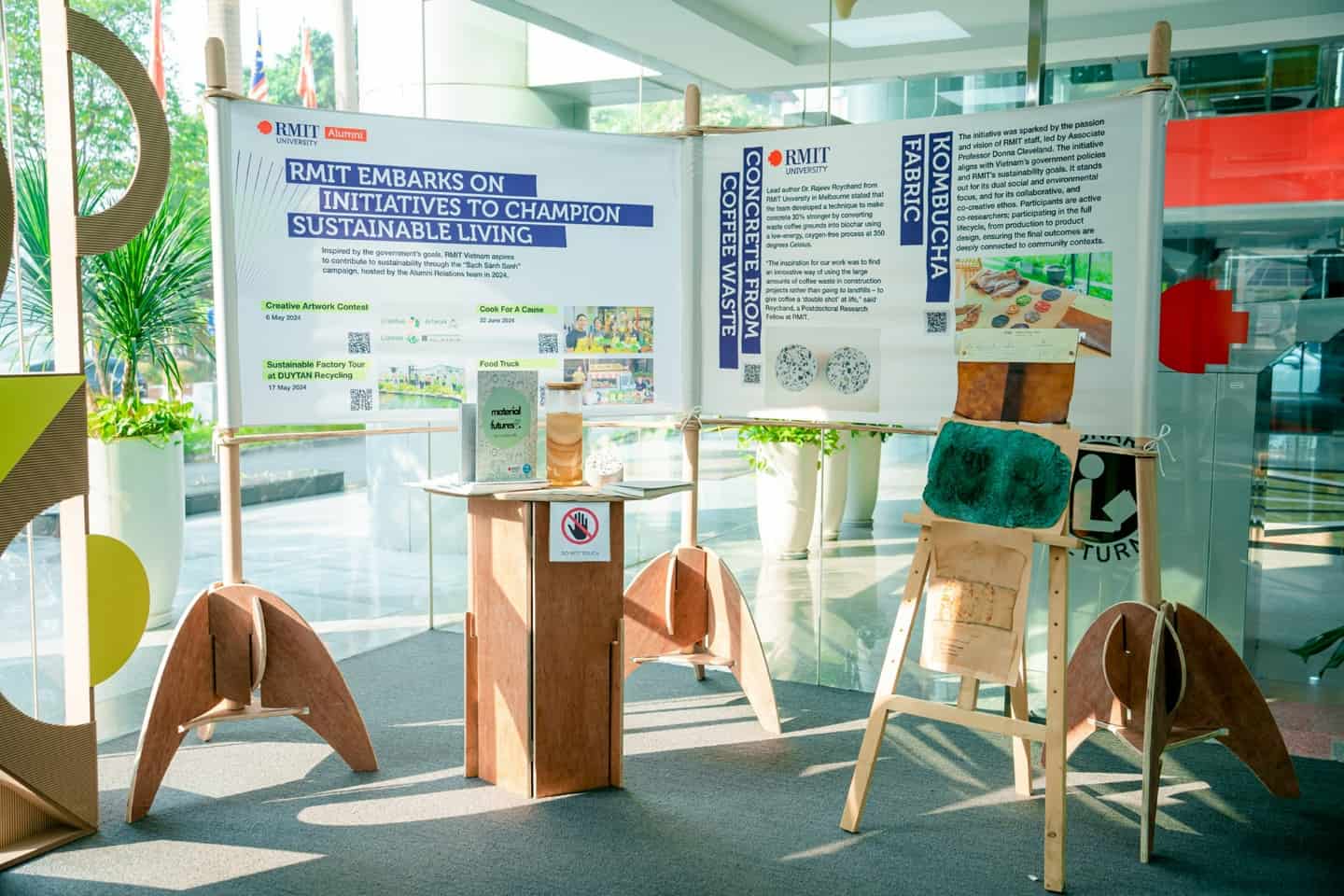 Display at an RMIT event highlighting initiatives for sustainable living, featuring projects such as creating concrete from coffee waste and Kombucha fabric, with posters and sustainable materials exhibited.