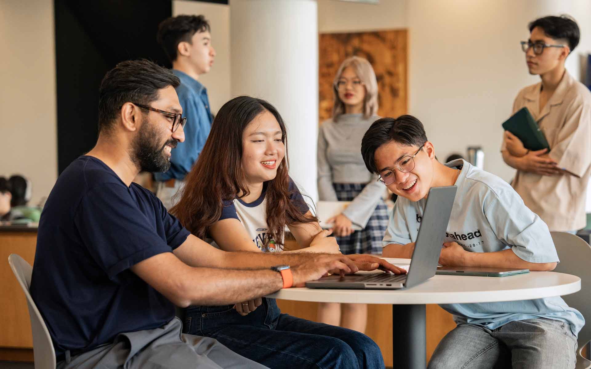 a group of students sitting on a campus lobby and looking at a laptop screen to discuss their content