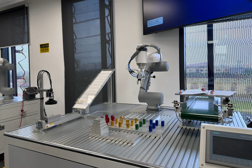 Photo of RMIT lab setup features a robotic arm positioned on a metal surface, surrounded by colorful objects and technical equipment