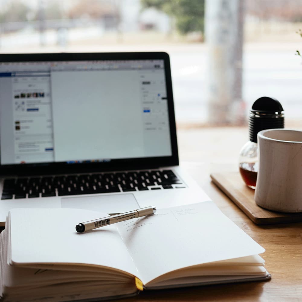 a pen on an opened notebook in front of a laptop