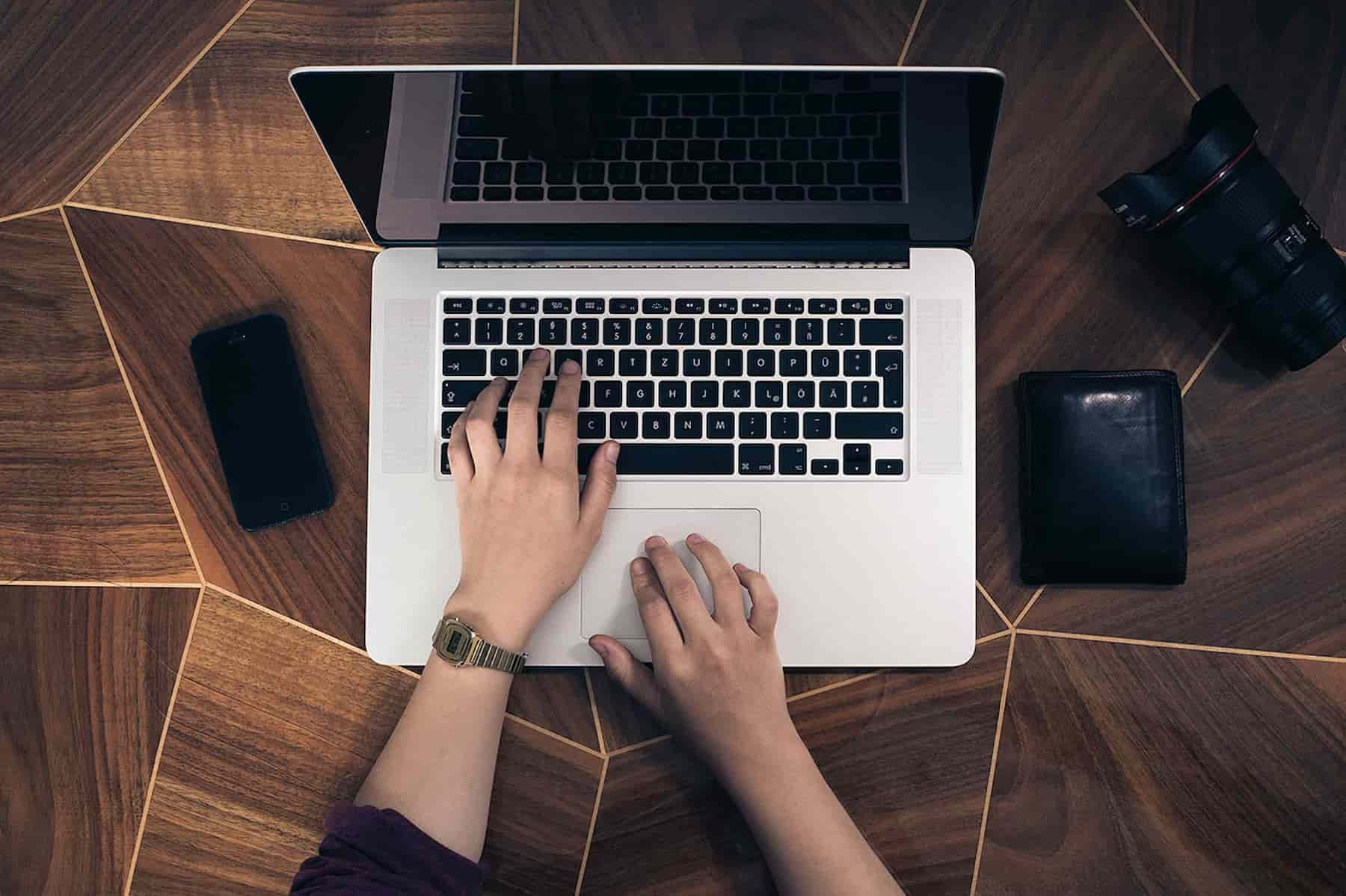 Hands on a laptop with a feature wooden desk, phone and wallet