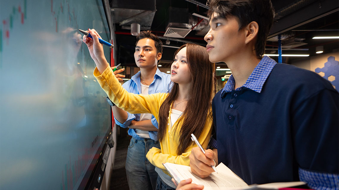 A student writing on the board and two other students looking at the board