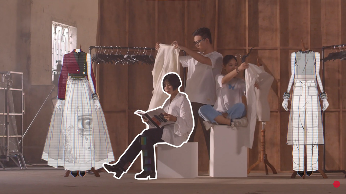 three students sitting and holding up clothes surrounded by two design drafts